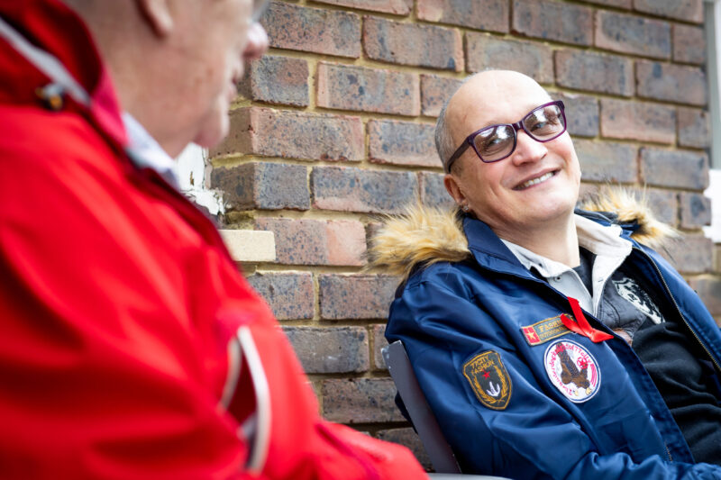 2 elderly men outside by a brick wall smiling