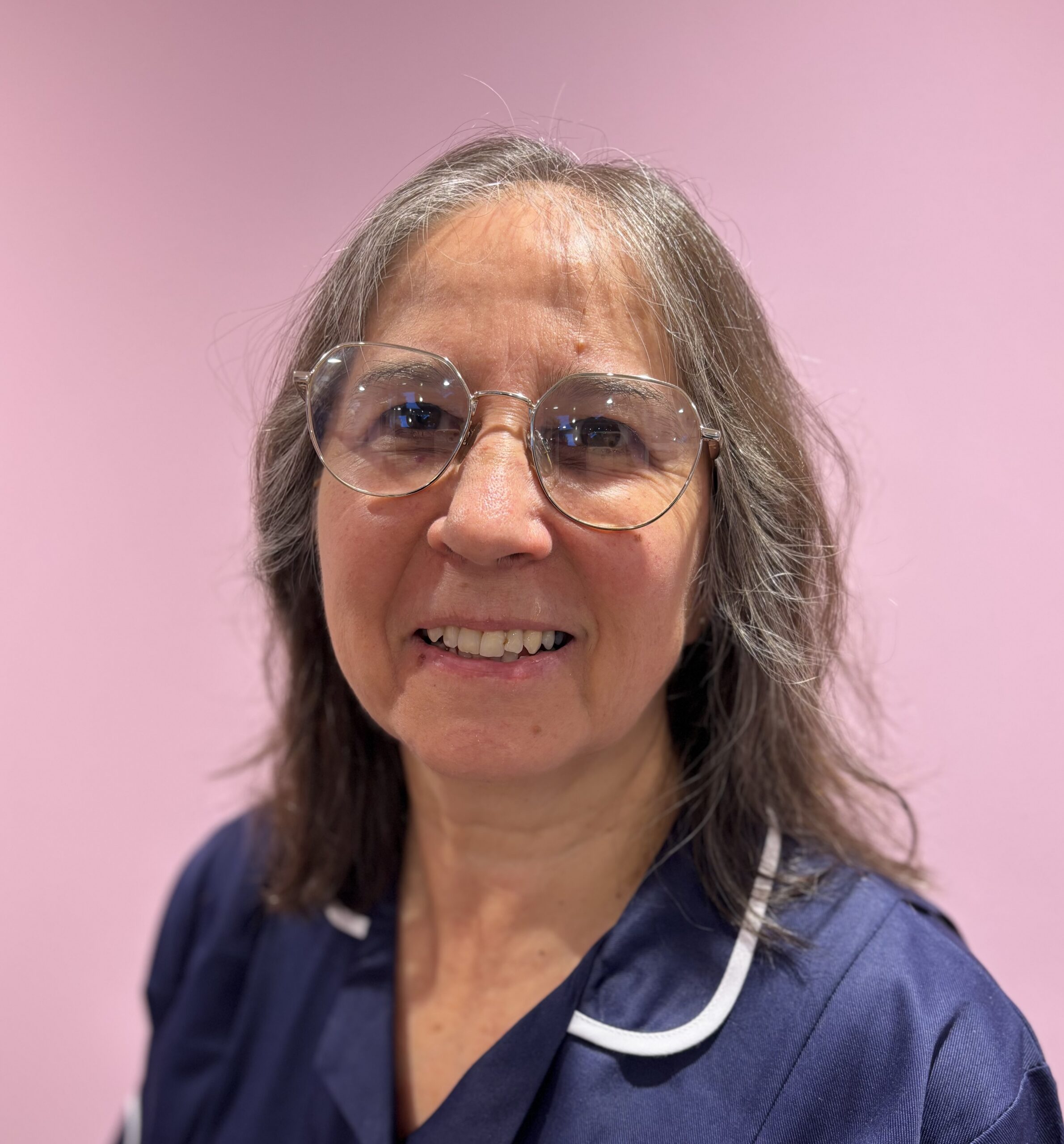 Photograph of female carer in uniform, with pink background 