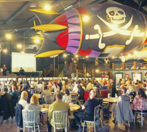 Employment is for Everyone launch event. Shows a room full of people sat around tables at a conference. Above them is an inflatable pirate blimp