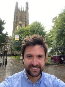 Photo of Tom Hughes smiling and stood in front of a church