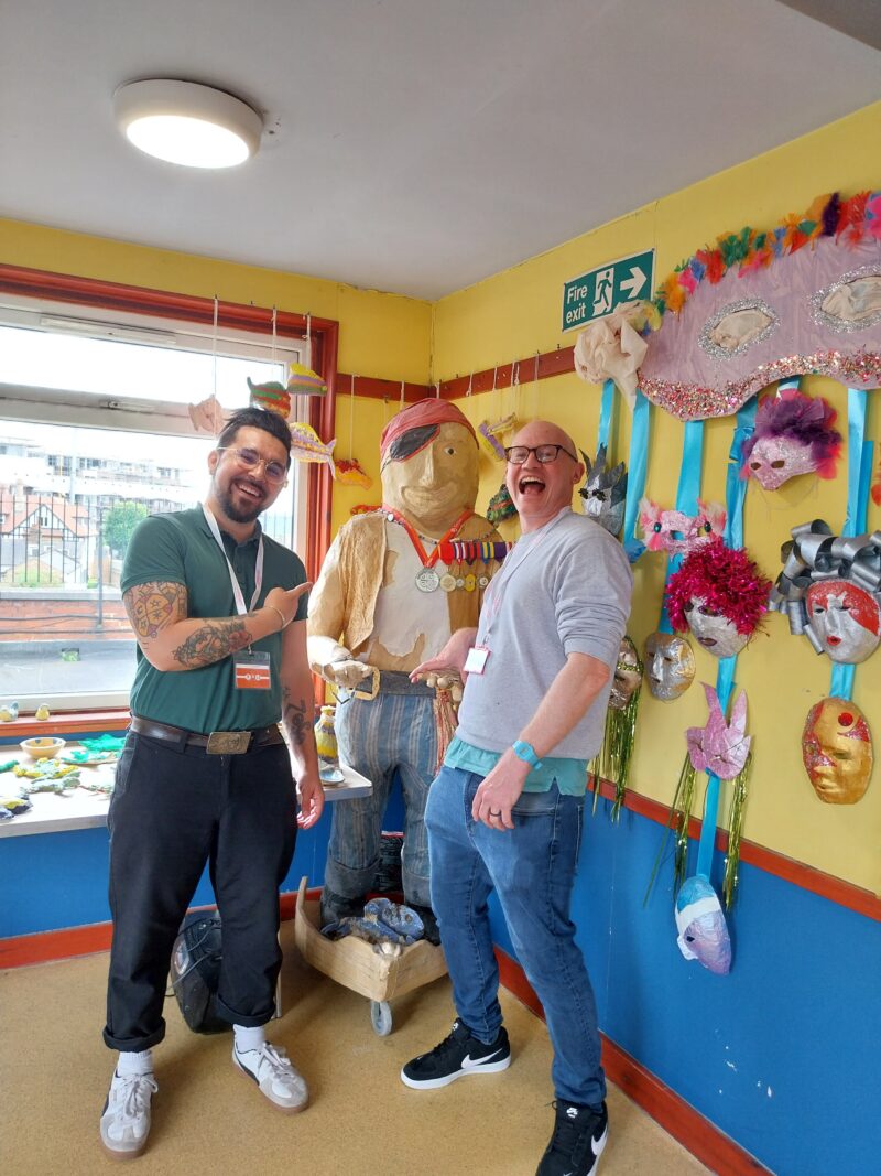 Two people standing and smiling a the camera in a colourful room