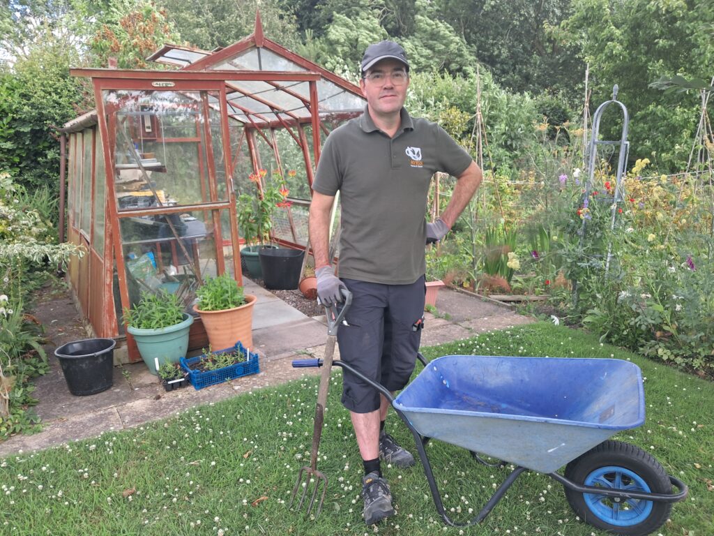 A man standing in a garden with a wheelbarrow.