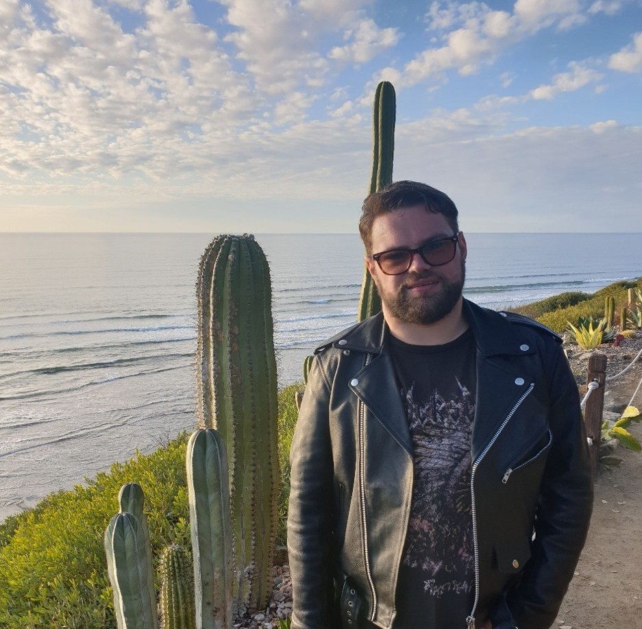 A man standing at a coastline beside a cactus tree